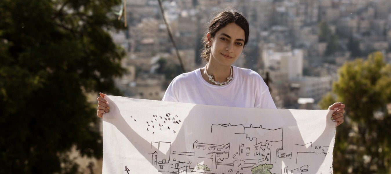 An artisan holding up a piece of white fabric with black embroidery.