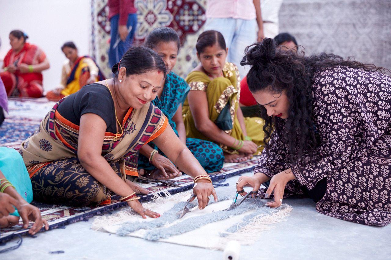 Designer Akanksha Deo and a group of women in traditional Indian clothes sitting on the floor working with textiles.