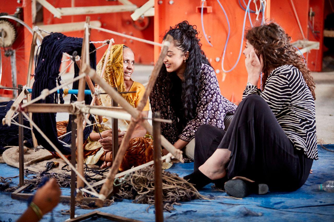 Three women sitting on a blue rug working with yarn and rope.