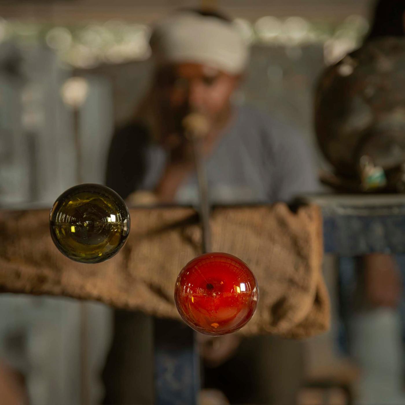 A person blows glass through a pipe.