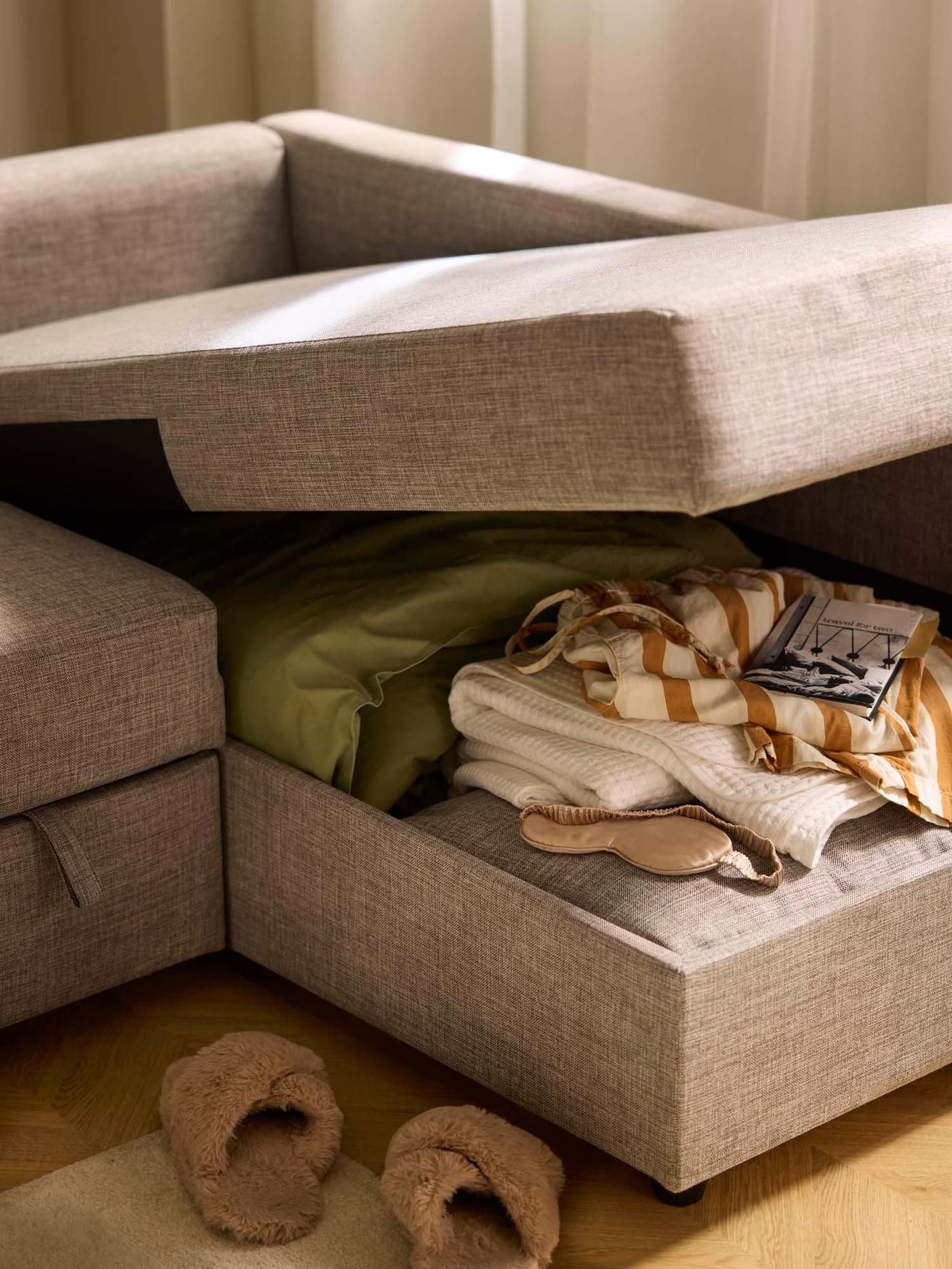 A grey sectional sofa with an open storage compartment holding blankets and clothing items.