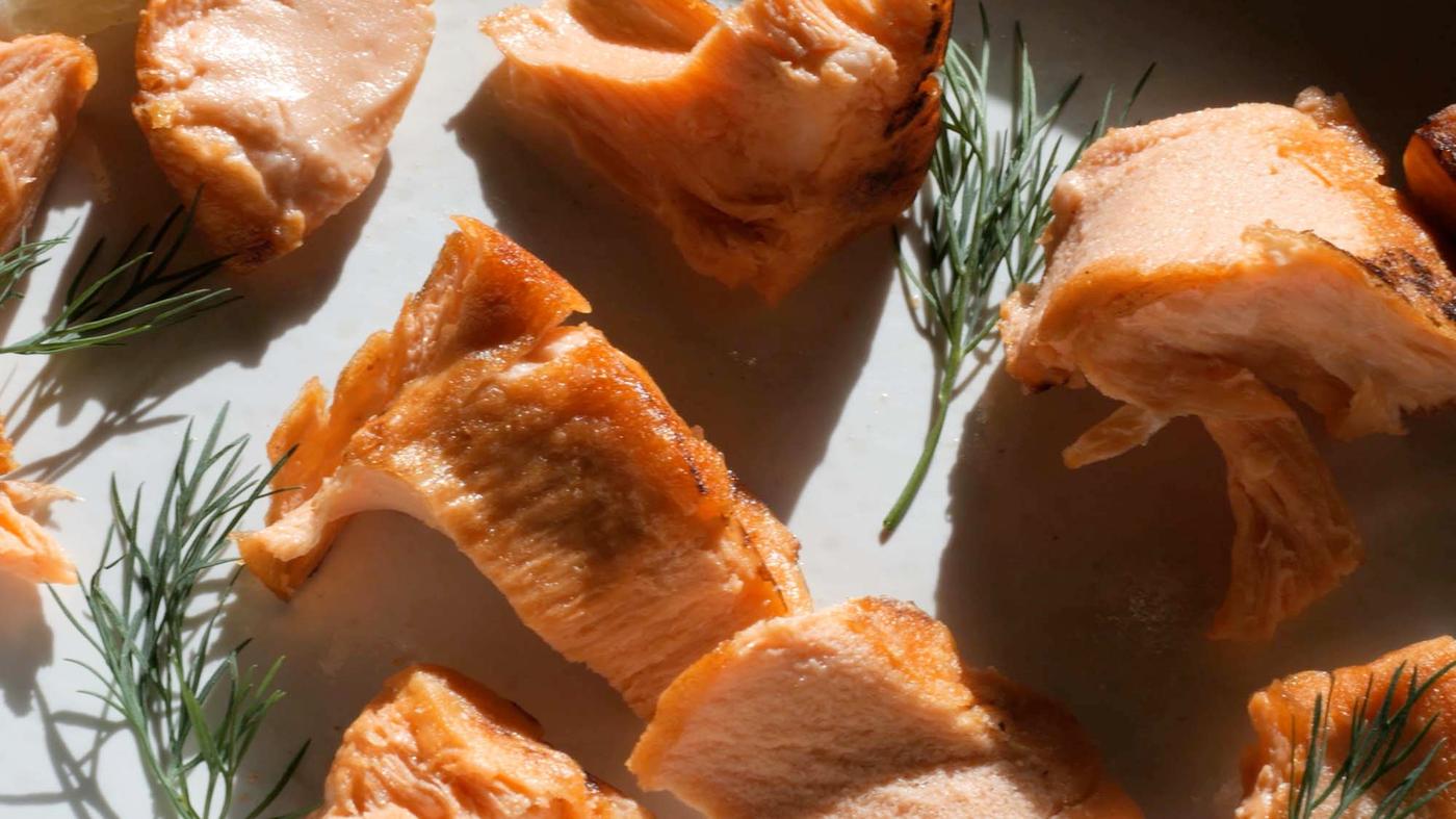 A plate with cooked chunks of New School Food plant-based salmon. The plate is decorated with herb garnish.