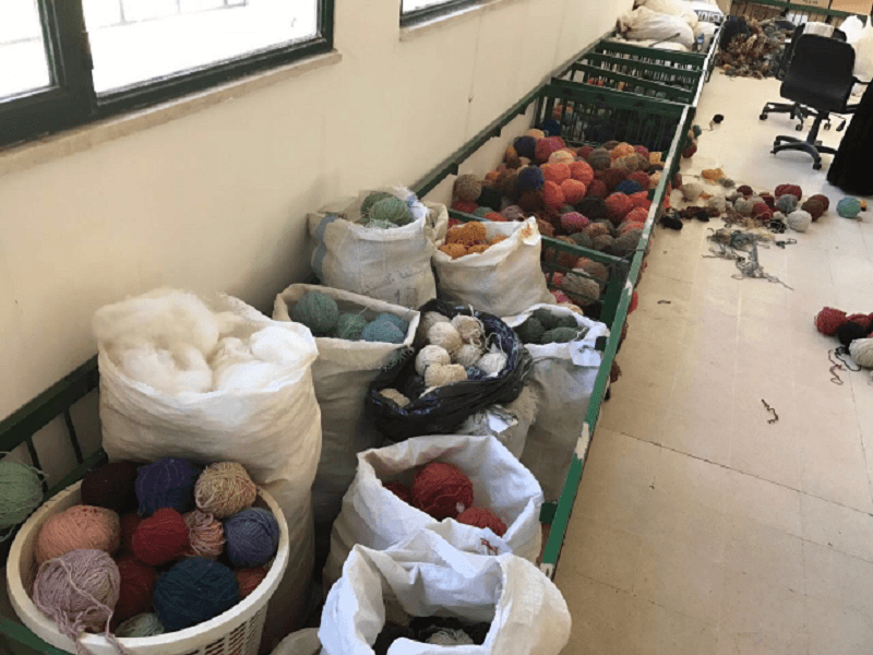 A room with a long bench with lots of balls of yarn in bags.