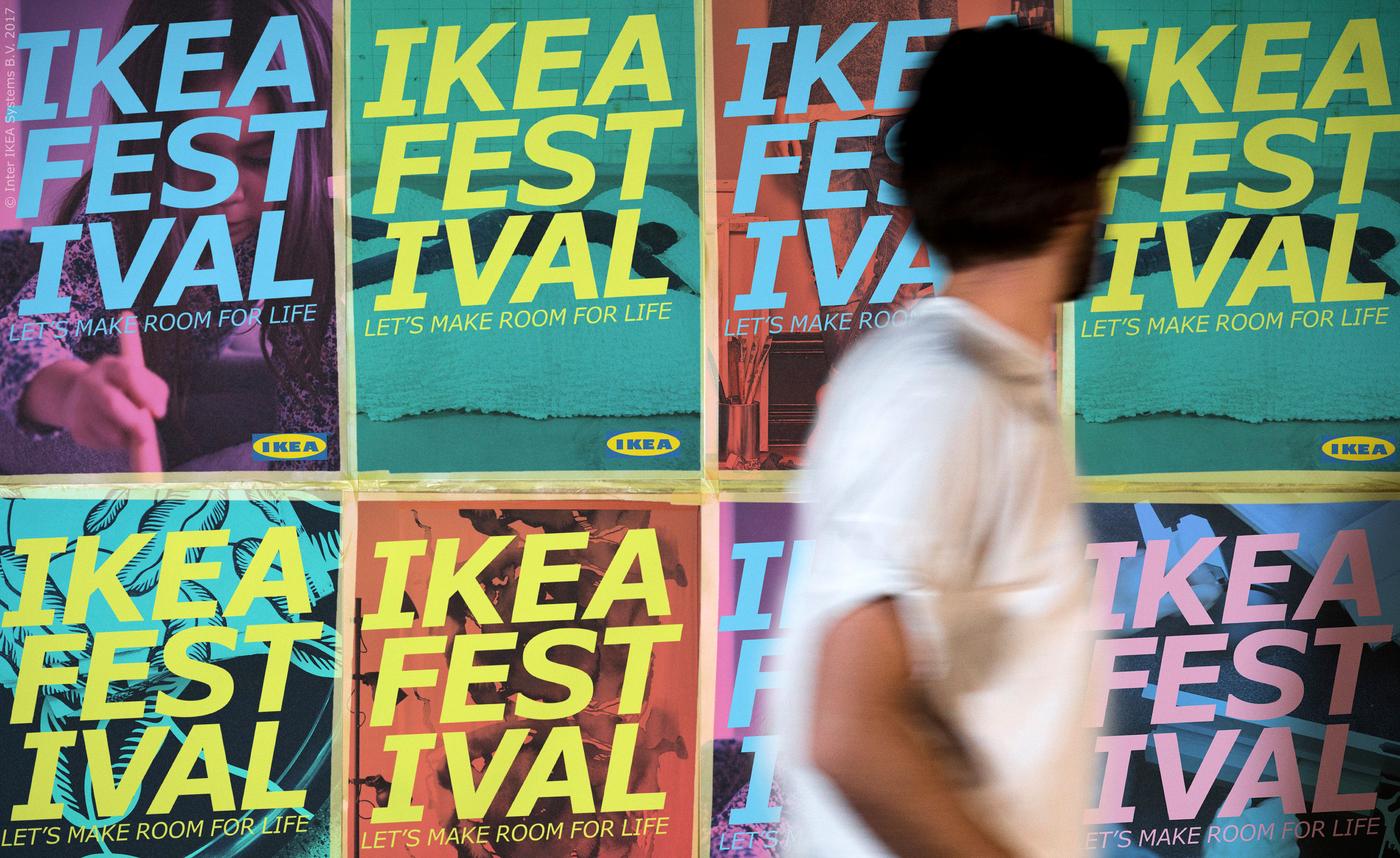 A person in a white top walks past a wall with 8 IKEA Festival posters taped on it.