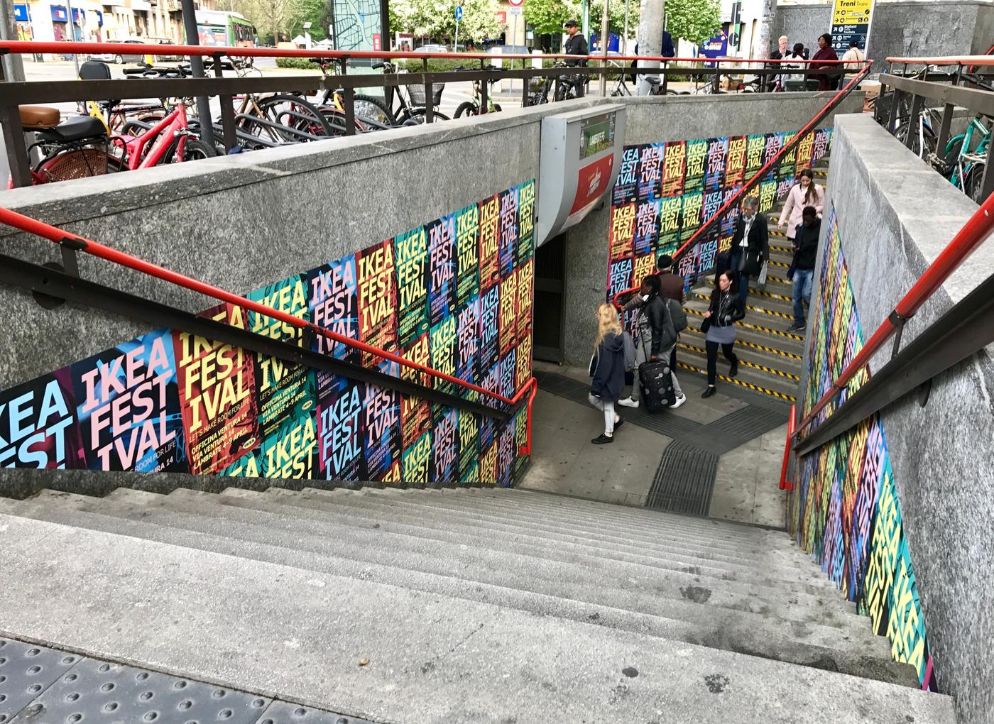 A concrete staircase leading down. There are handrails and posters on the walls.