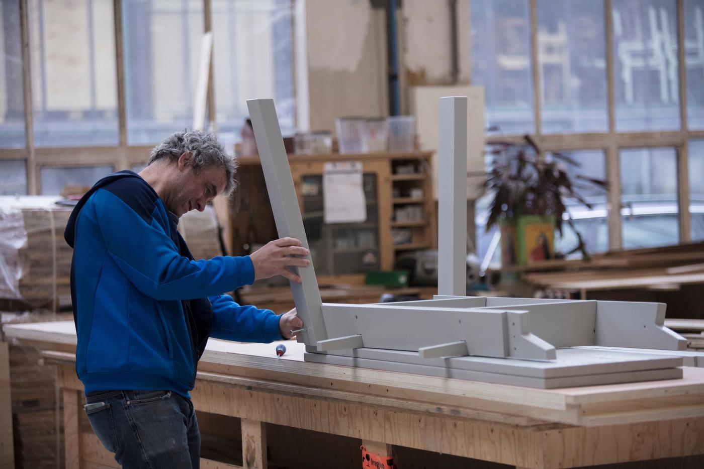 A man is building a grey table in a workshop.