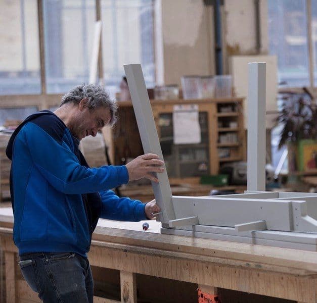 A man is building a grey table in a workshop.