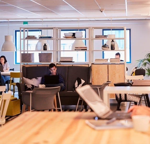 A person sits at a table working on his computer. He is wearing headphones.