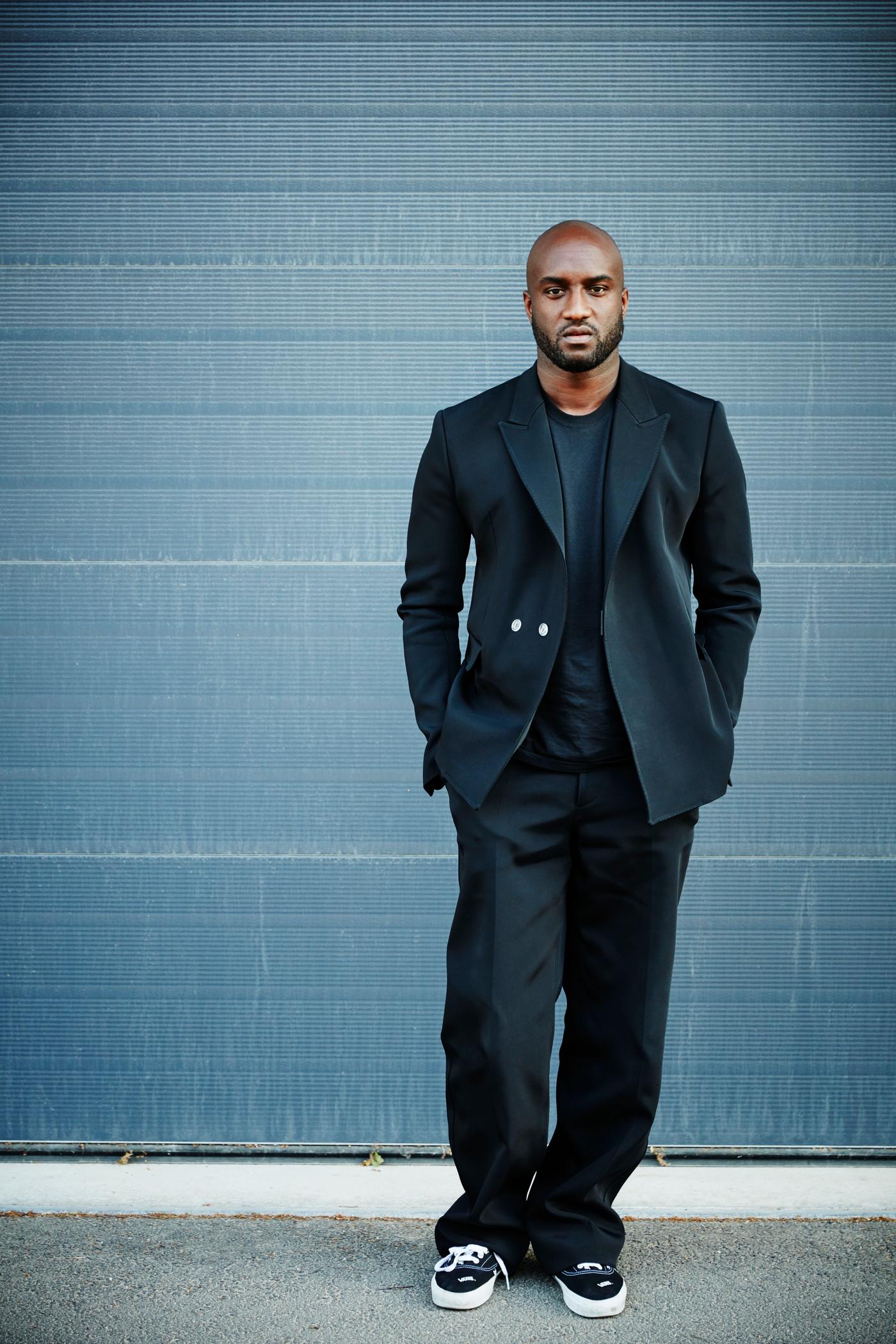 Virgil Abloh stands against a blue wall looking at the camera.