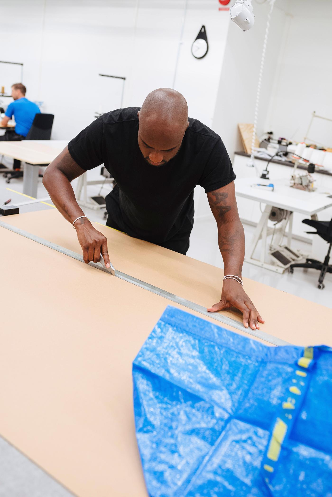 Virgil Abloh makes measurements on a sheet of material with a blue FRAKTA bag nearby on the work surface.