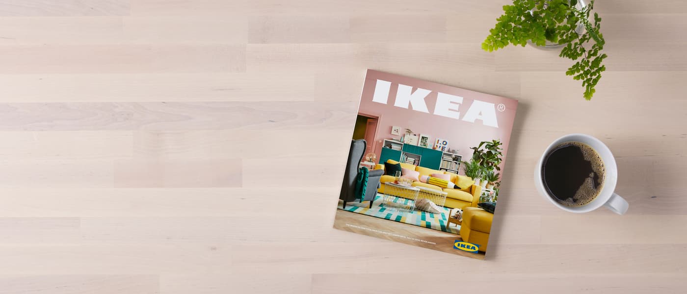 A wood surface with the 2018 IKEA Catalogue and a cup of hot beverage.