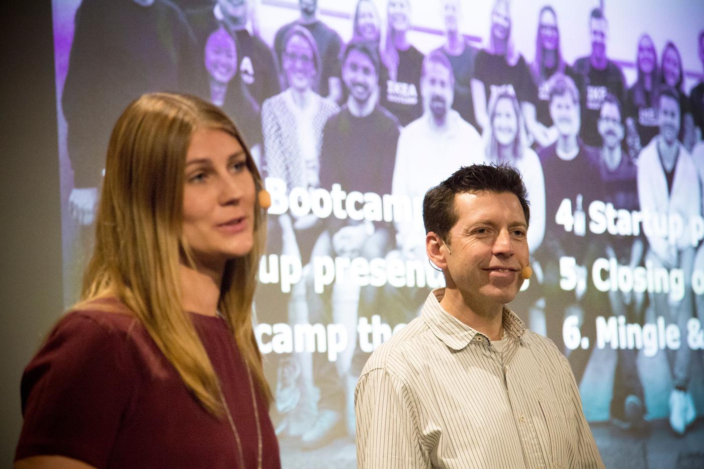Two people standing in front of a digital screen.