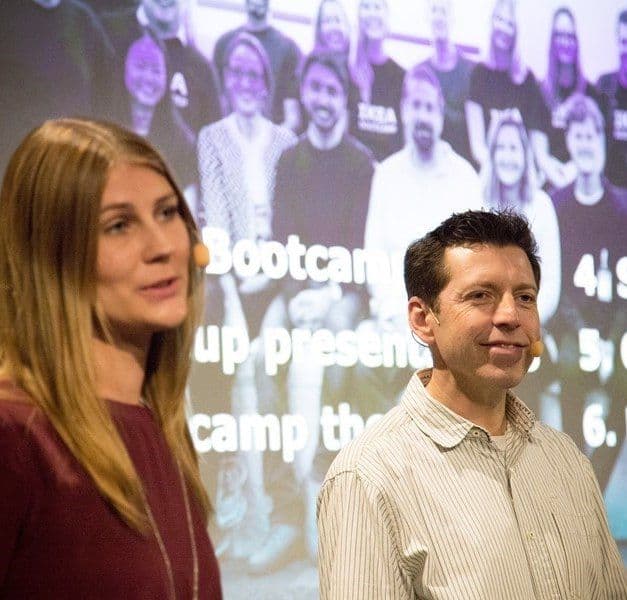 Two people standing in front of a digital screen.