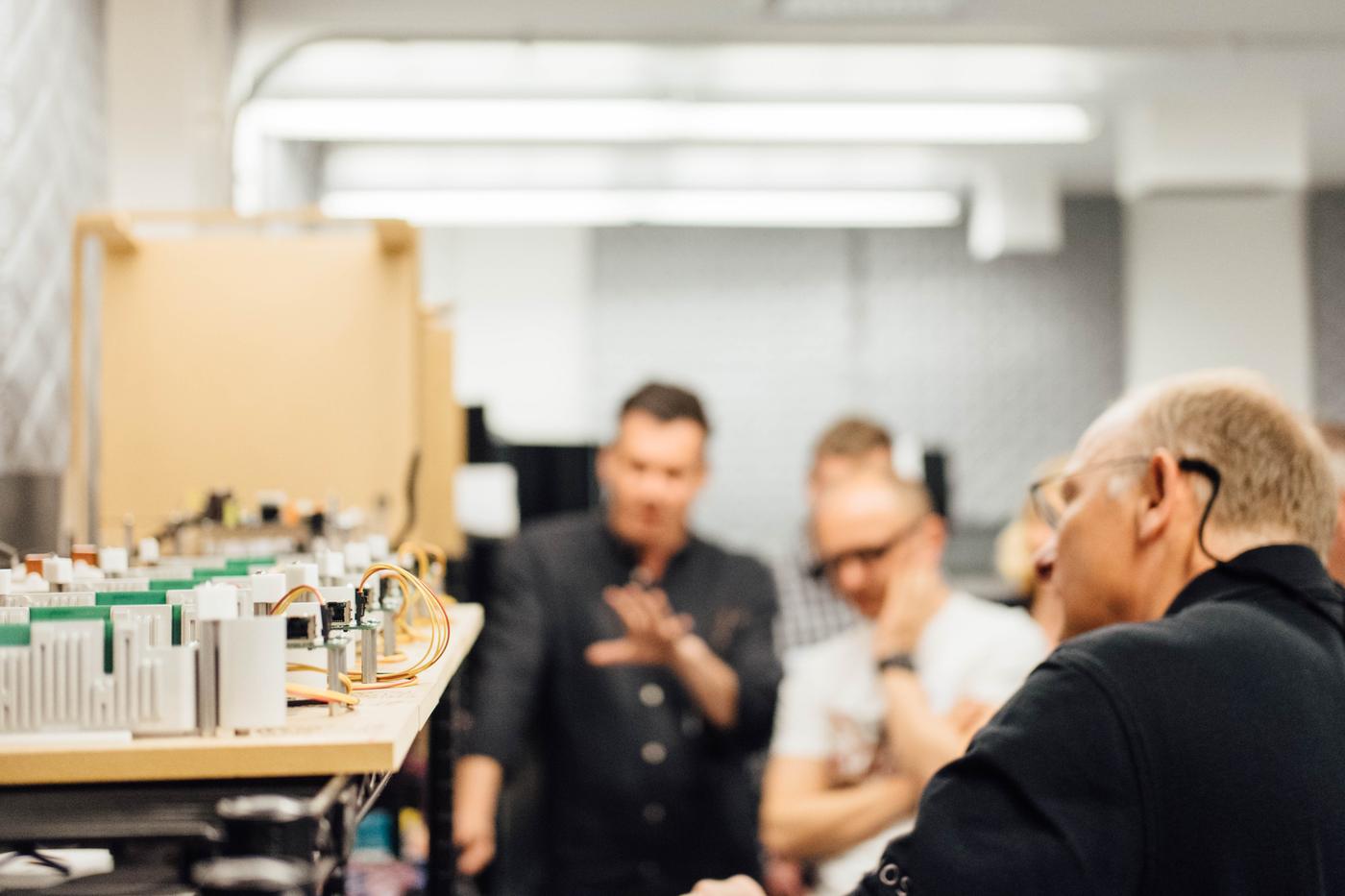 Three men look at electronic components and discuss.