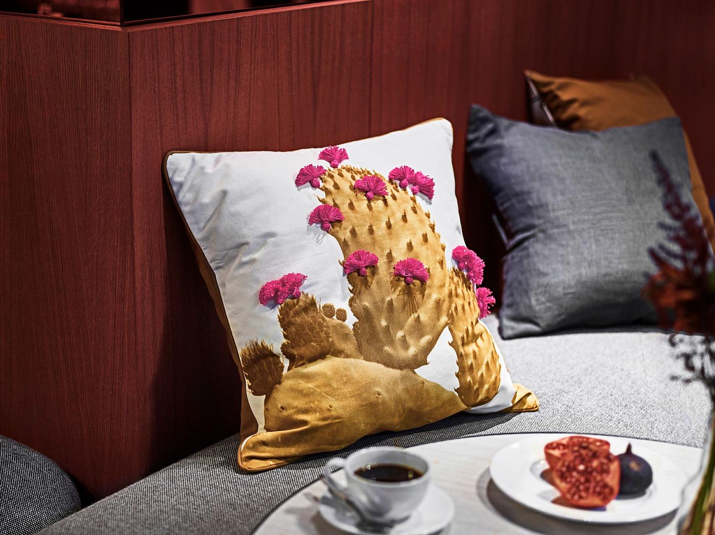 A cactus cushion on a bench, next to a table with a cup of hot beverage.