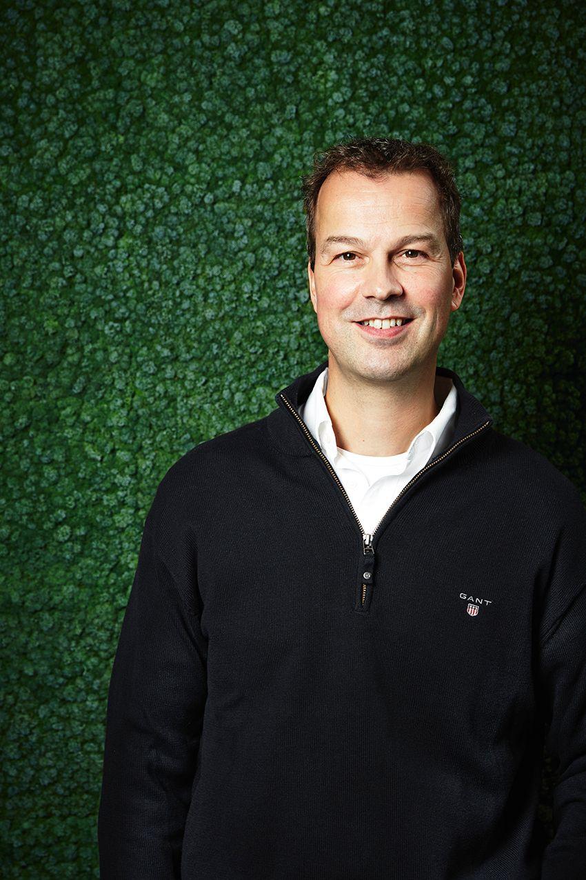 Portrait of Peter van der Poel standing against a green wall of plants.