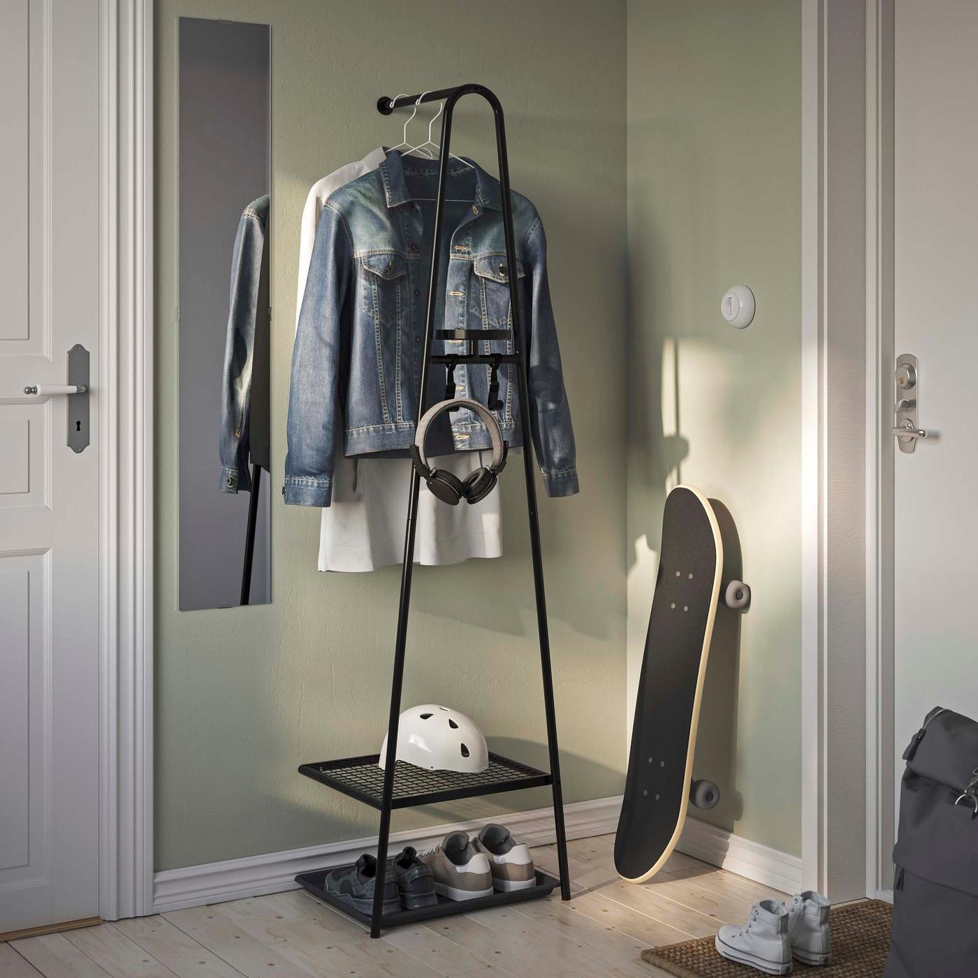 An entryway with a black metal clothes stand where a jacket and helmet are hung. The clothes stand has shelves at the bottom for storage and is part of a space-saving design for organising clothing and accessories.