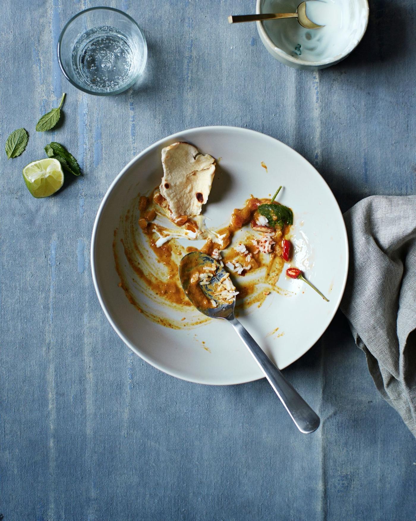 A bowl with food and a spoon on a grey tablecloth covered surface.