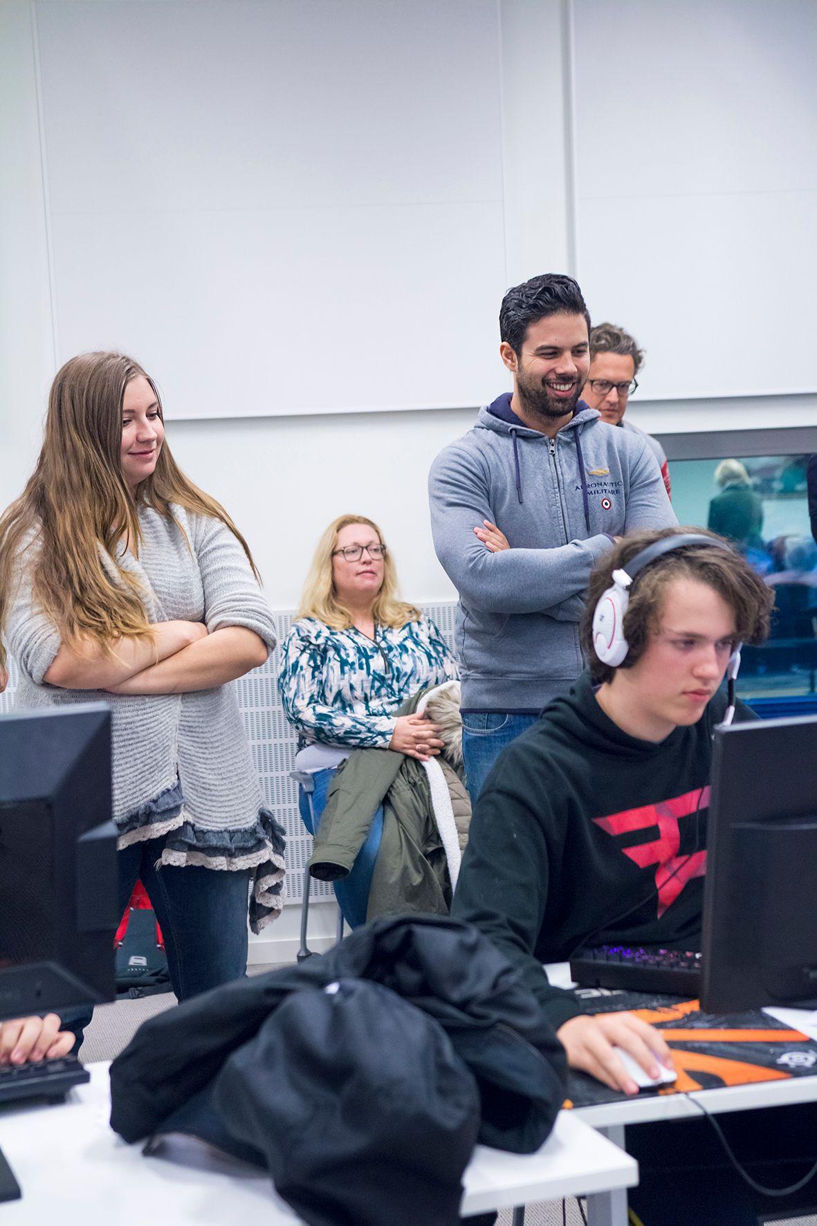 A group of people stand and watch a person gaming at a desk.