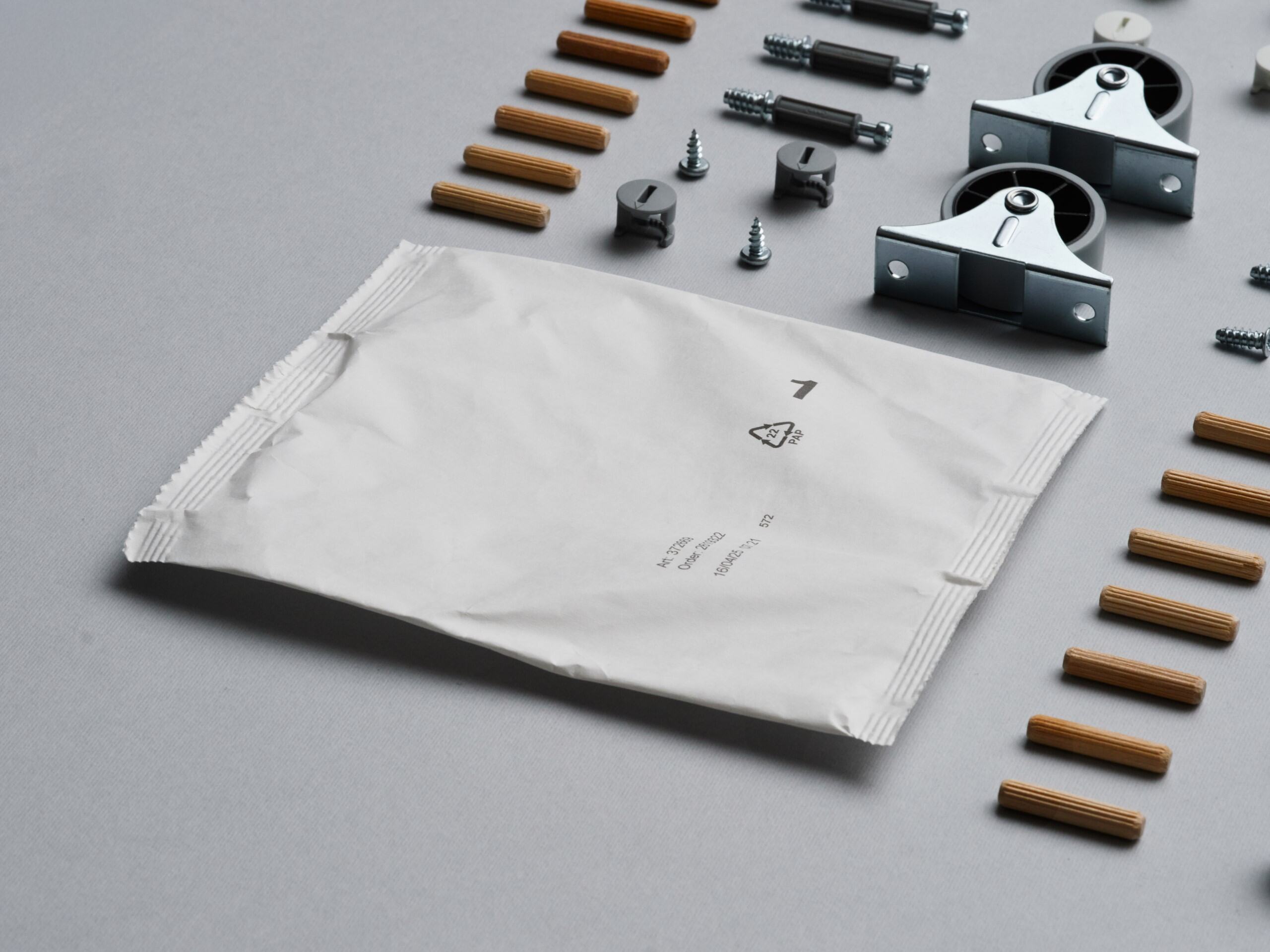 A paper-based fitting bag lies flat on a grey surface with various spare parts lined up next to it.