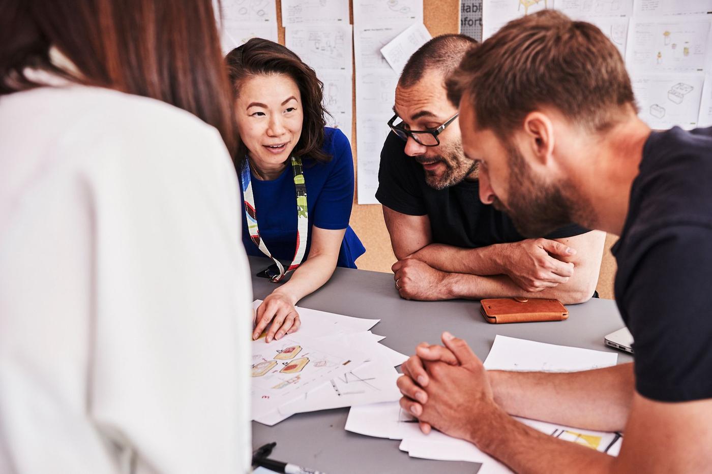 Group of people gathered around a table with many papers on the worktop and pinned to the walls around them.