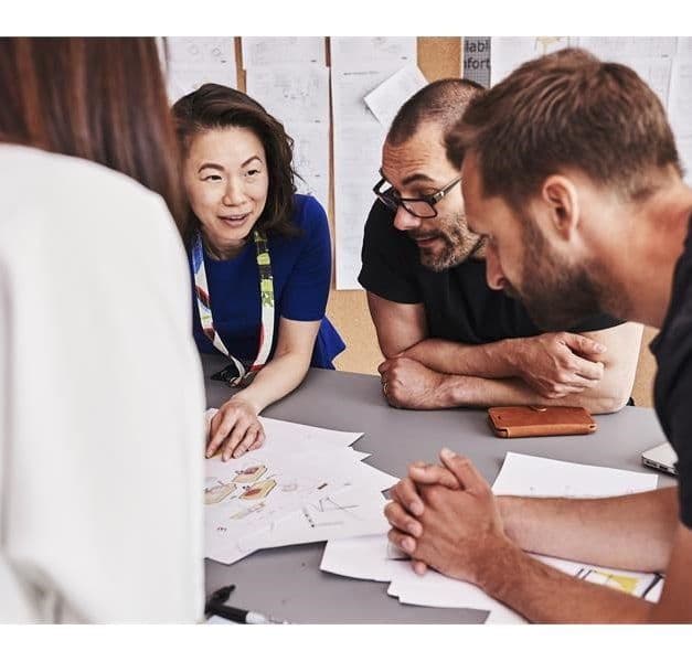 A group of people stand at a table brainstorming.