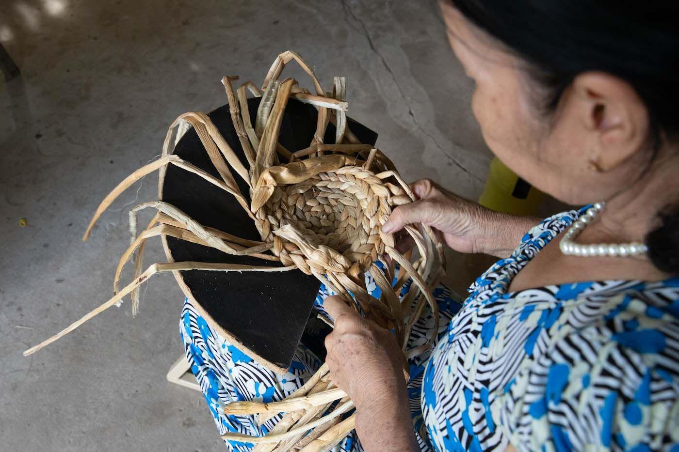 A person weaves a basket from dried leaves.