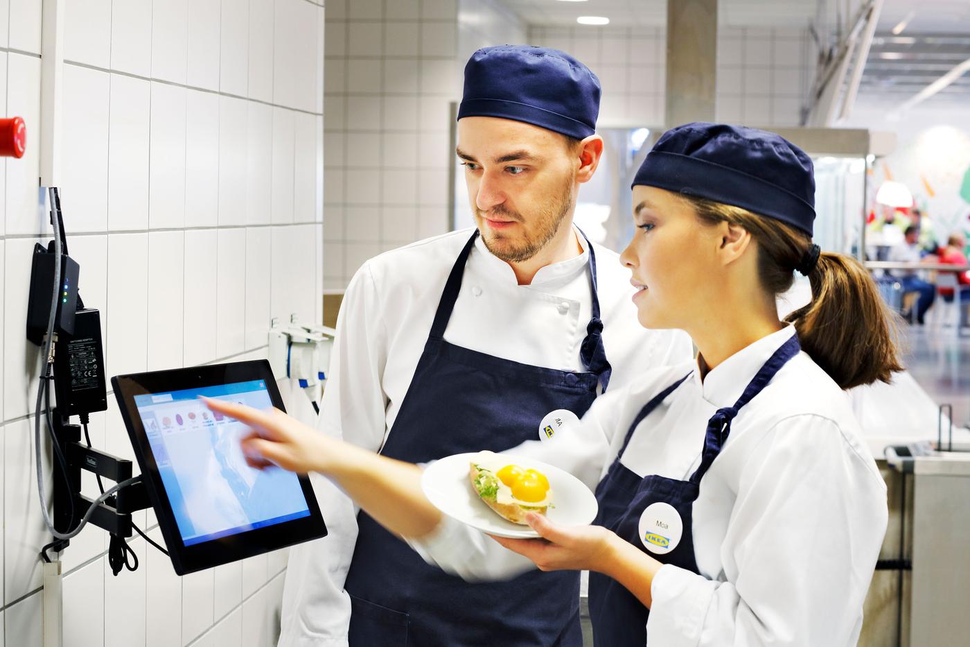 Two IKEA co-workers weigh waste food and register it on a computer screen.