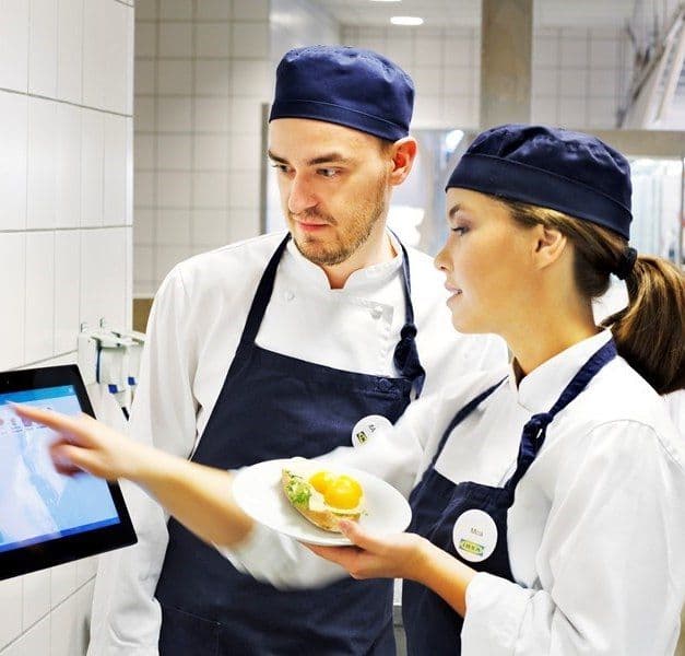 Two IKEA co-workers weigh waste food and register it on a computer screen.