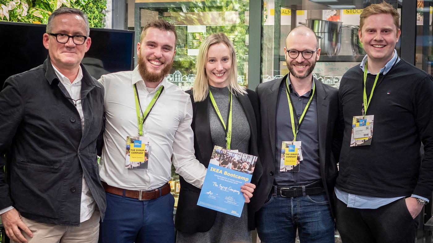 Four men and a woman smile at the camera. The woman is holding a certificate.