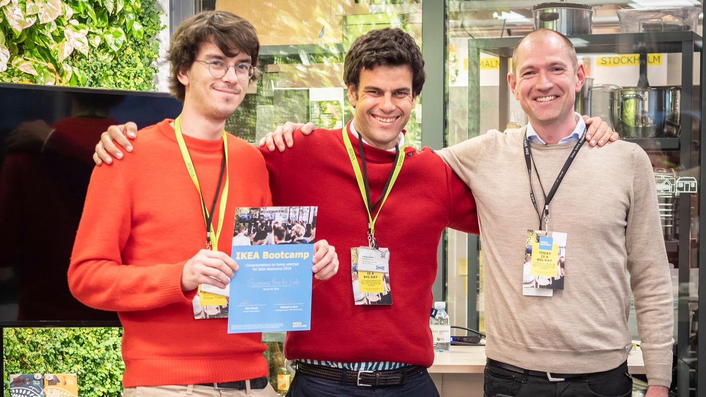 Three men smile at the camera. One is holding a certificate.