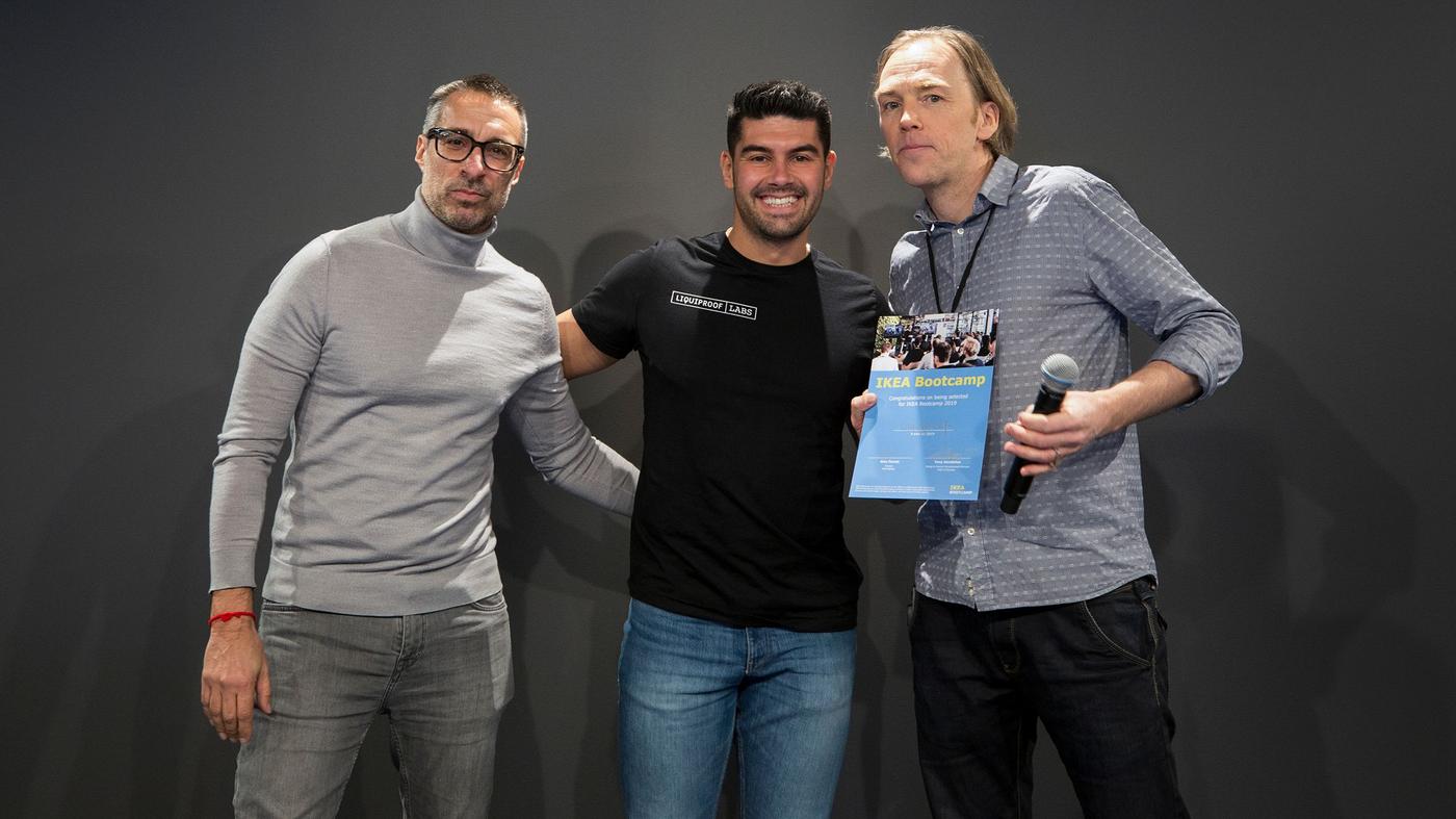 Two men smile at the camera. One is holding a microphone and a certificate.