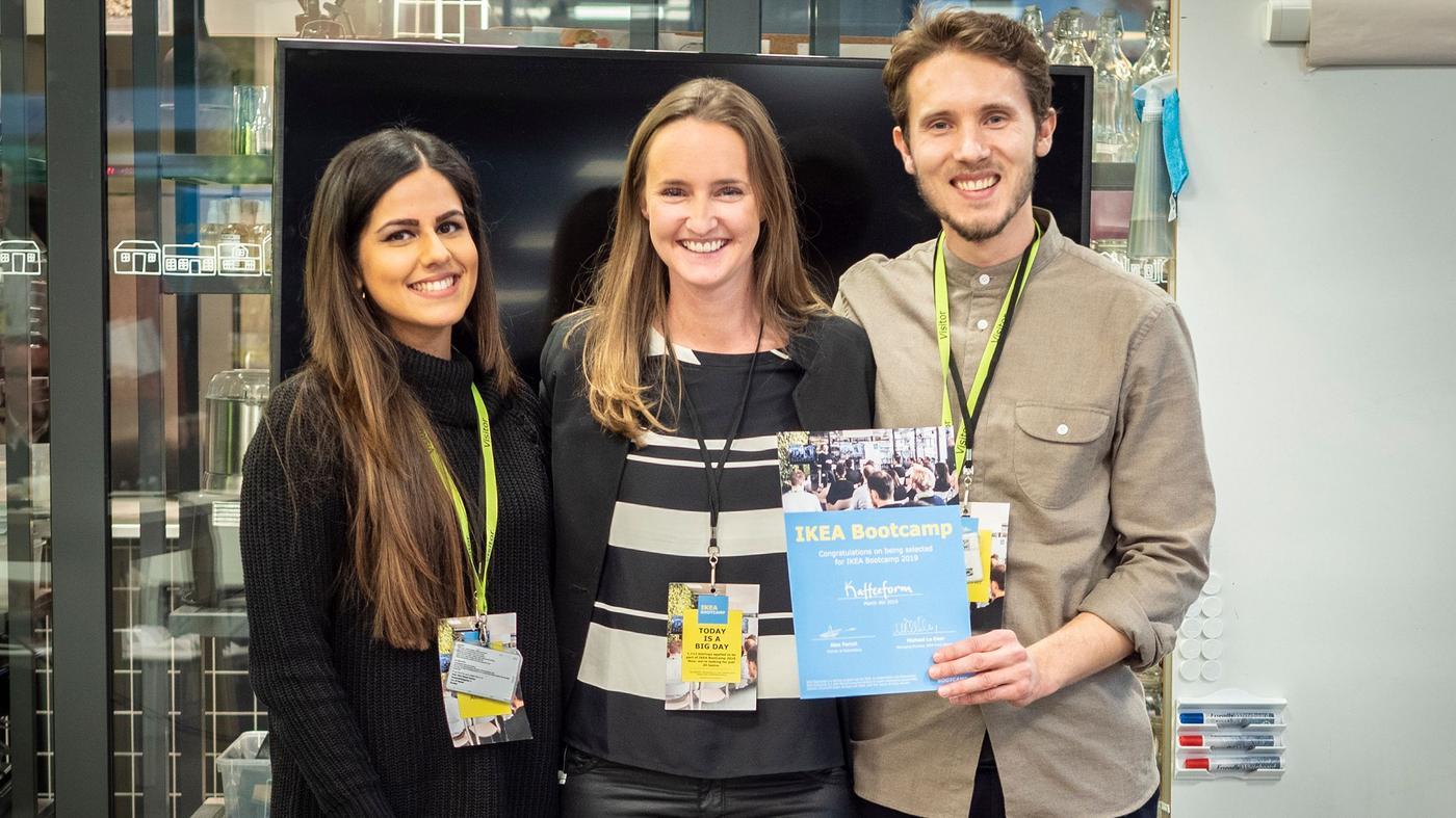 A man and two women smile at the camera. The man is holding a certificate.