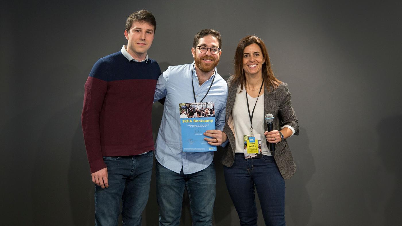 Two men and a woman smile at the camera. The woman is holding a microphone, the man holds a certificate.