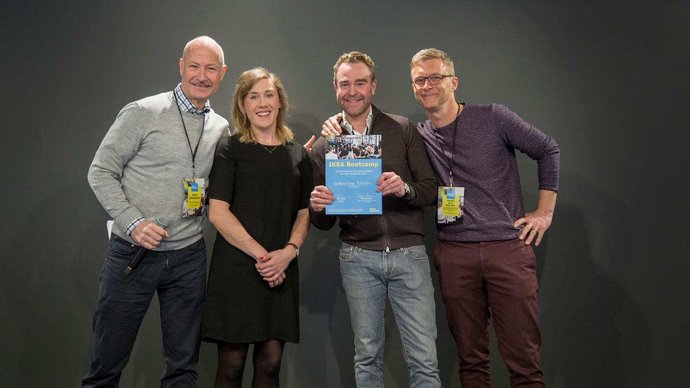 Three men and a woman smile at the camera. The man is holding a certificate.