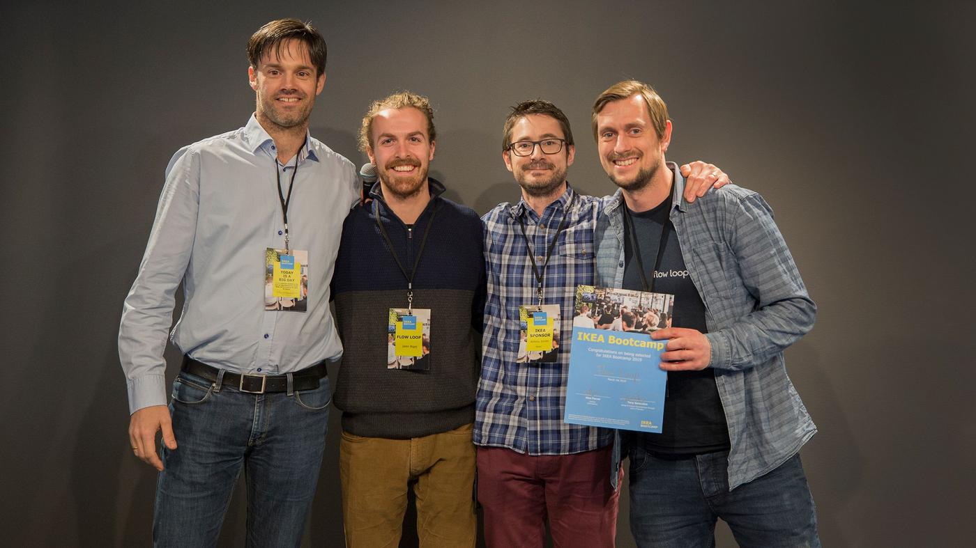 Four men smile at the camera. One is holding a certificate.