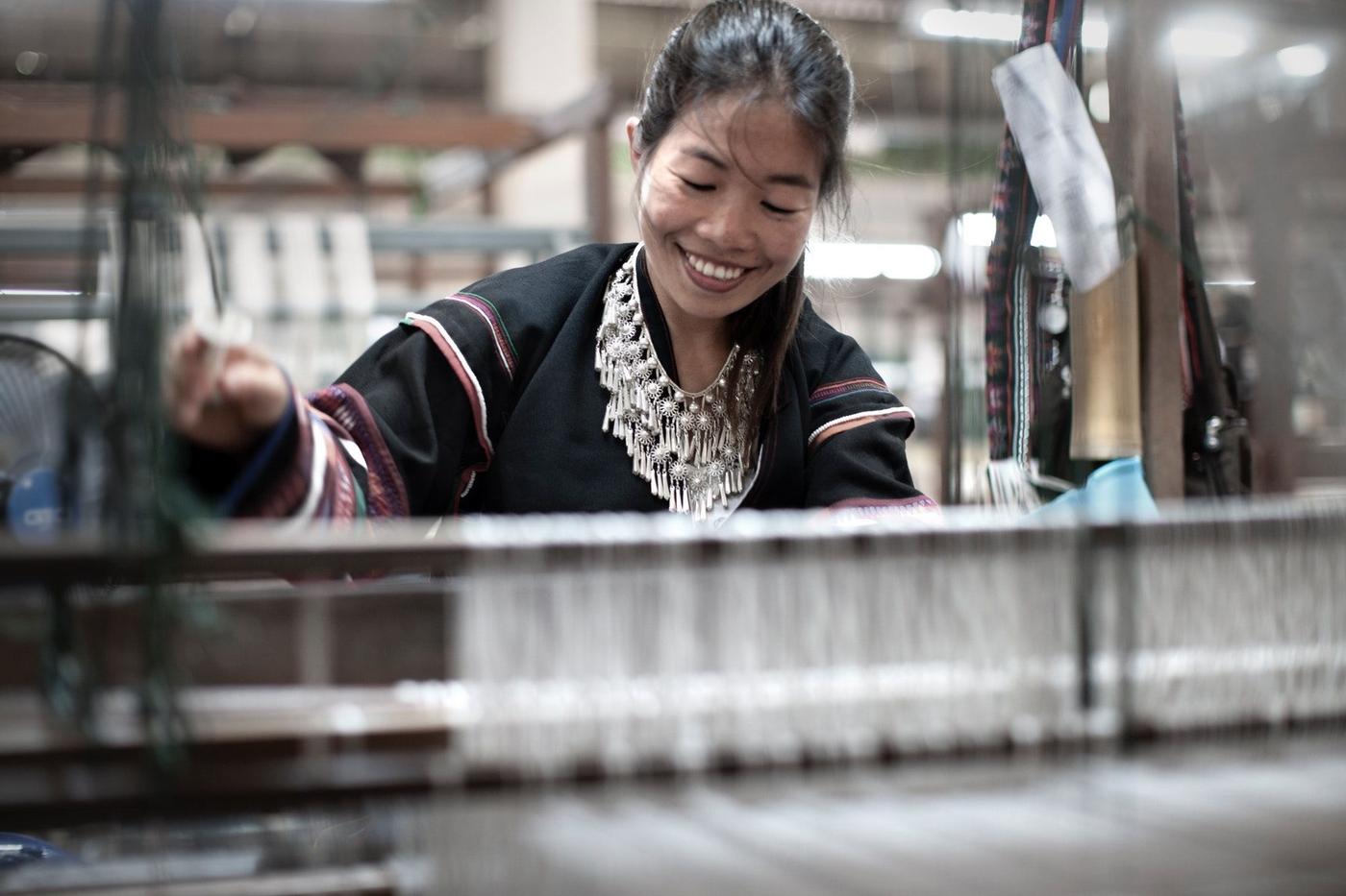 An artisan working with loom and smiling.