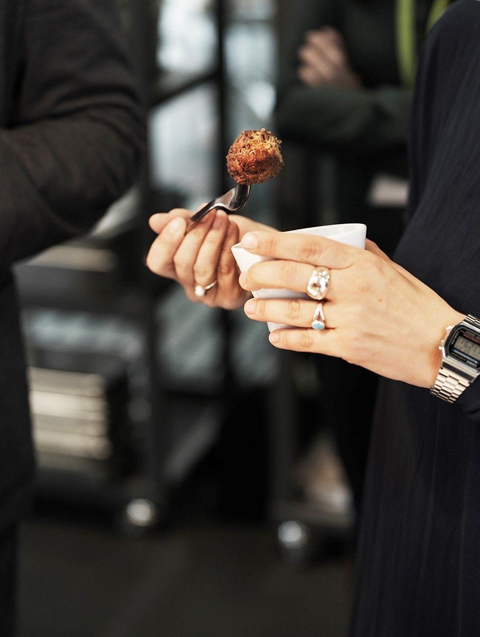 A hand holds a bowl, while the other hand holds a fork with a plant-based meatball.