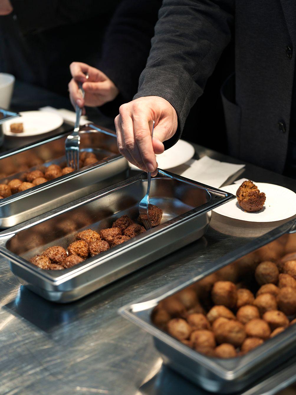 In a canteen, a person helps themself to plant-based meatballs.