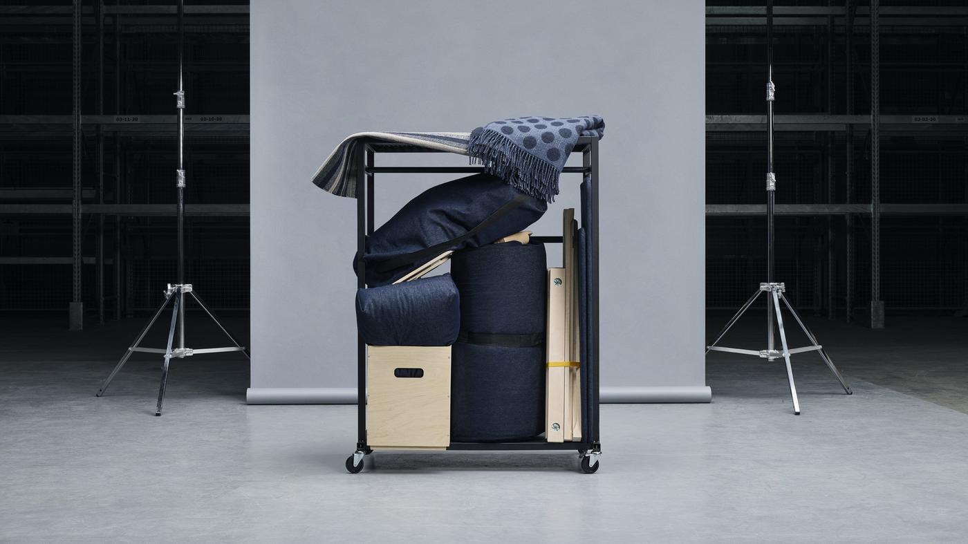 A disassembled sofa with dark-grey cushions, a wooden storage box, a striped rug and a dotted blanket packed on a trolley.
