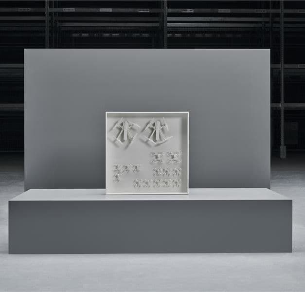 A design object comprising of white drones arranged in a white container on display on a grey plinth.
