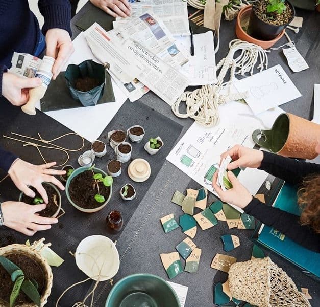 People gathered around a worktop full of sketches, colour swatches and seedlings being potted in newspaper strips.