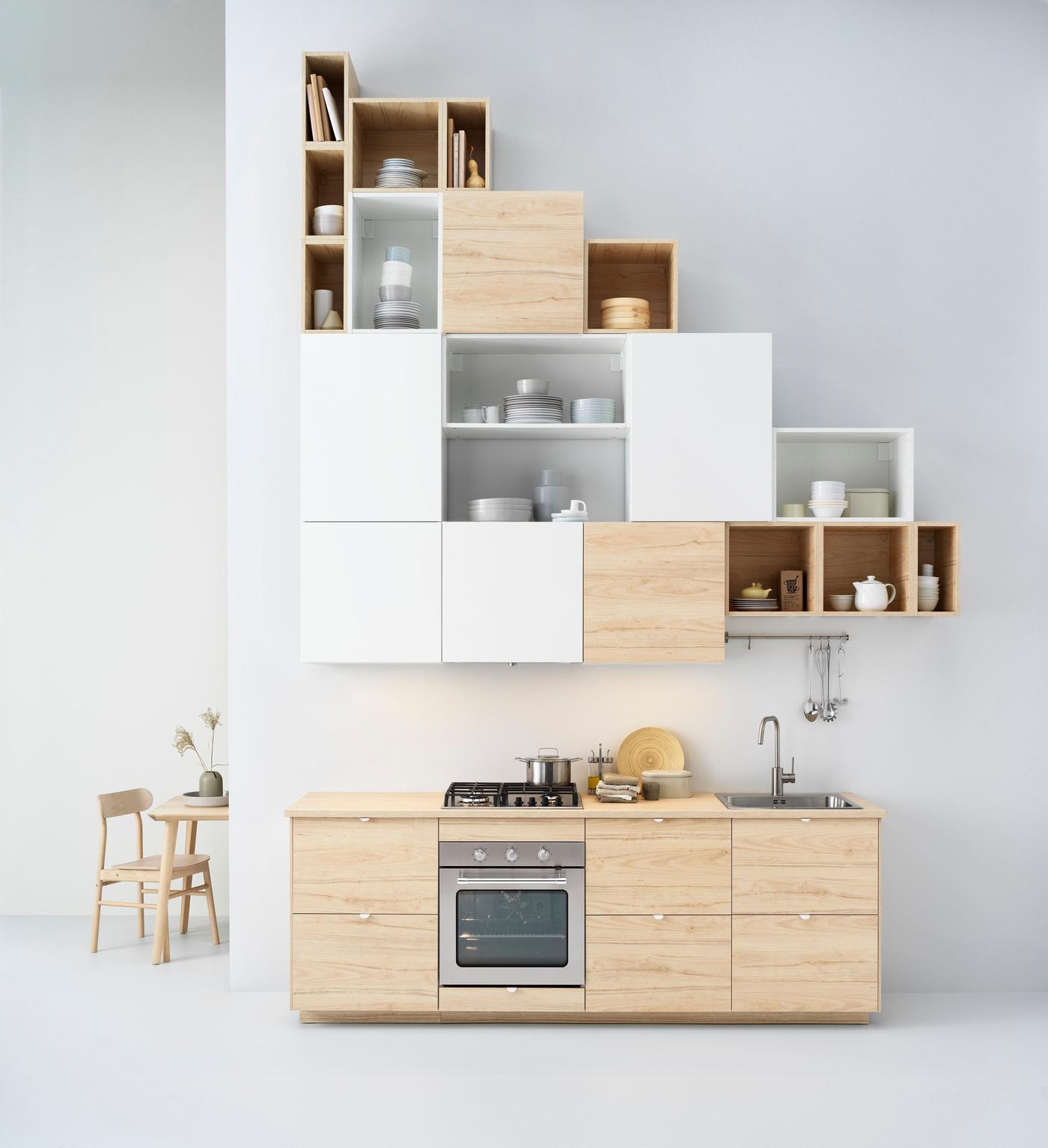 Compact kitchen with a short row of cabinets in light wood, with a striking, triangular shaped solution of high, wall-mounted cabinets above. 