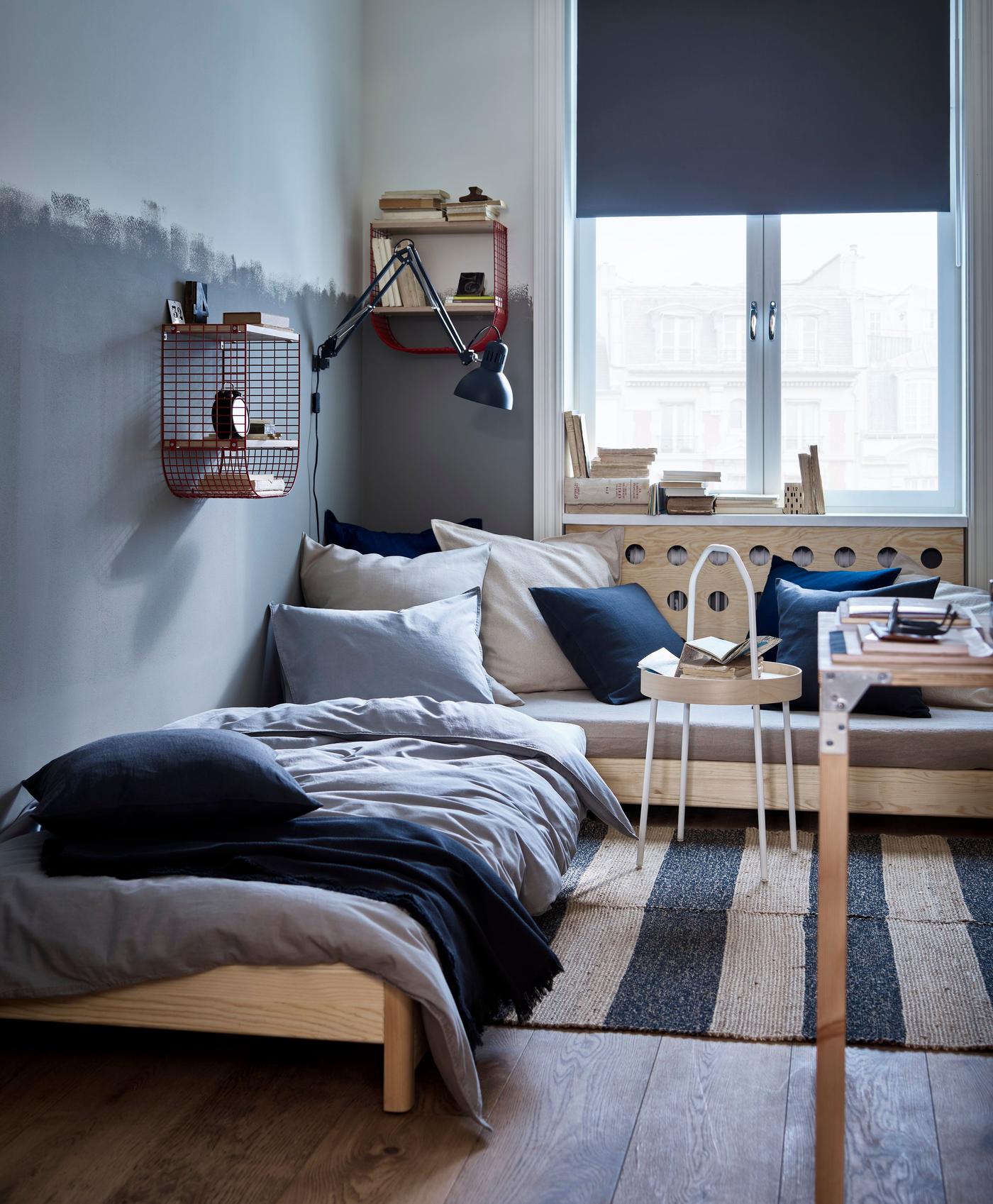 Bedroom with grey painted halfway up the walls and two low single beds placed together at a right angle in the corner of the room.