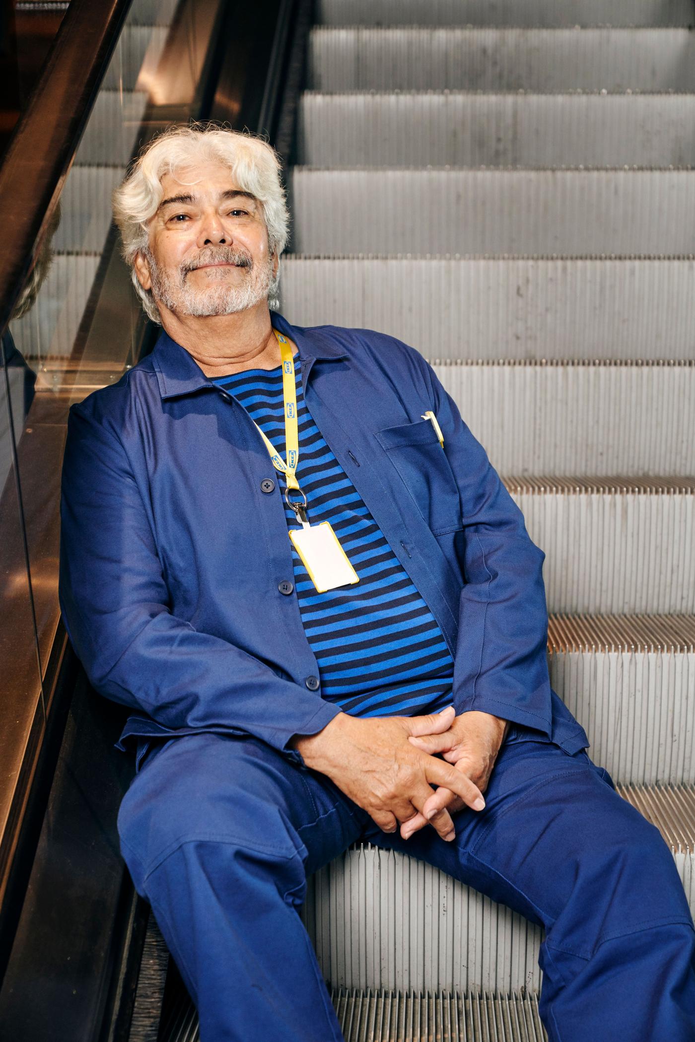 A man sits on a staircase. He is wearing blue trousers and jacket and a striped blue top.