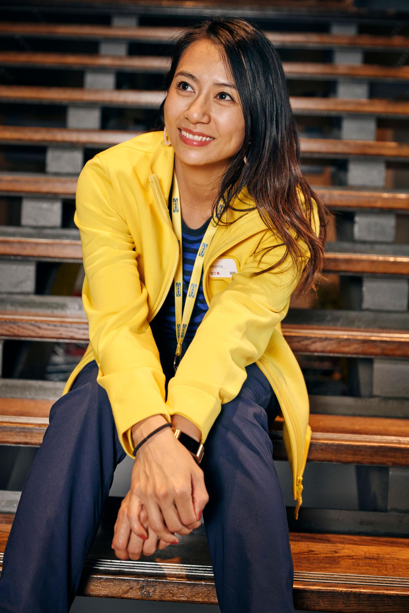 A woman sits on a wooden staircase. She is wearing navy trousers and a yellow jacket.