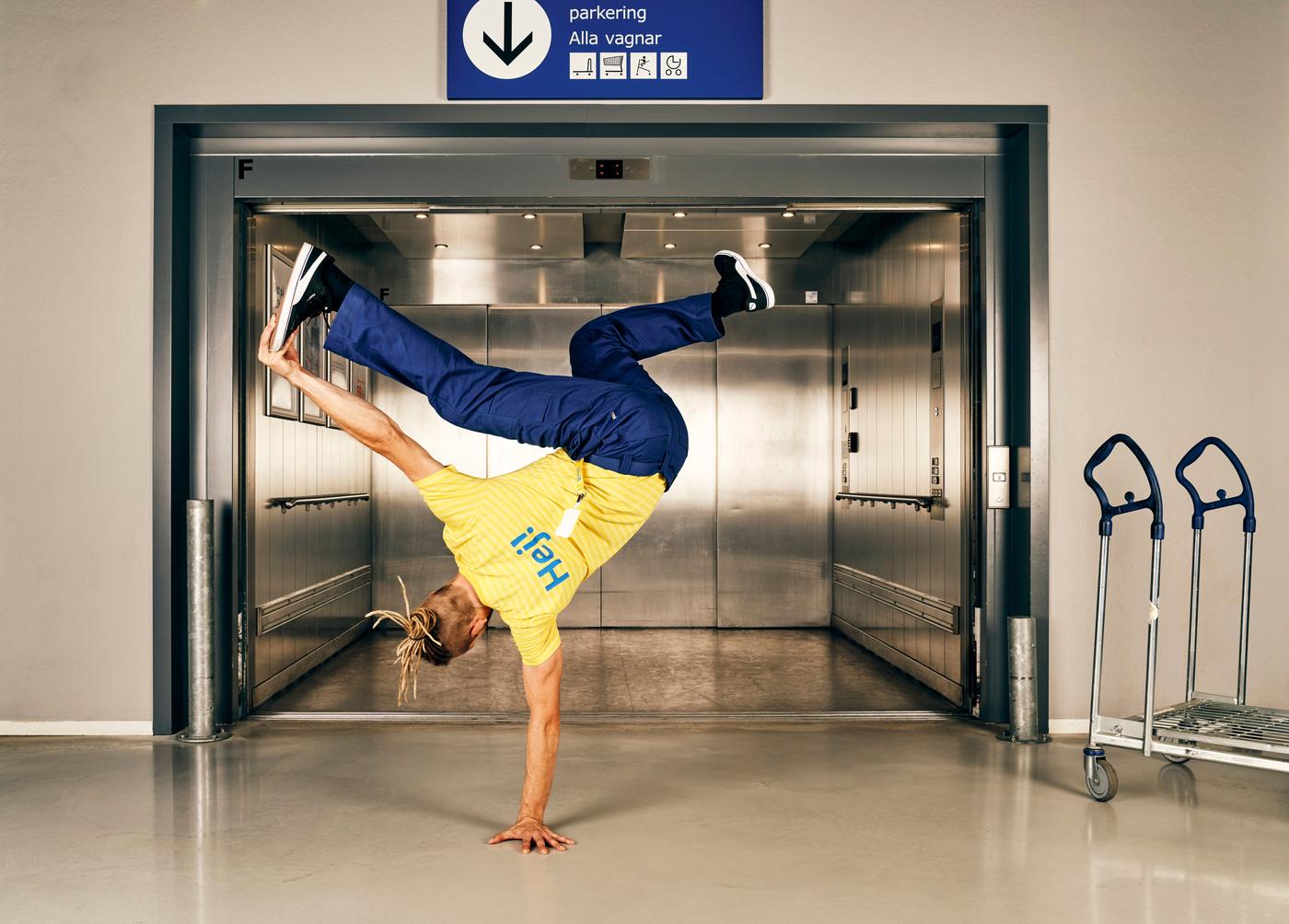 A man stands on one hand, while holding his foot in front of a lift in an IKEA store.