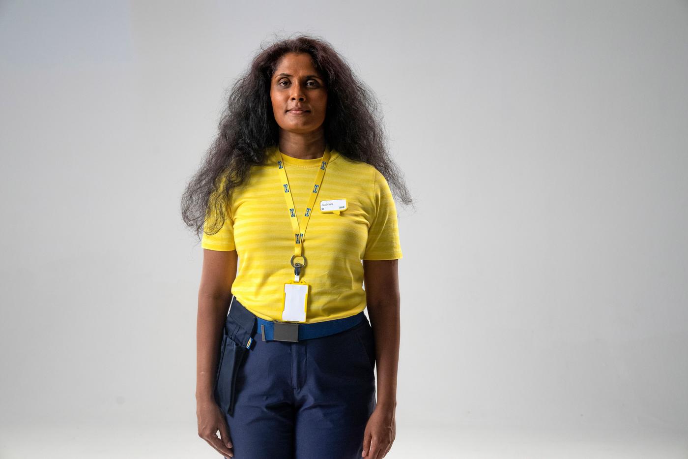 A woman looks at the camera. She is wearing a yellow t-shirt and lanyard.