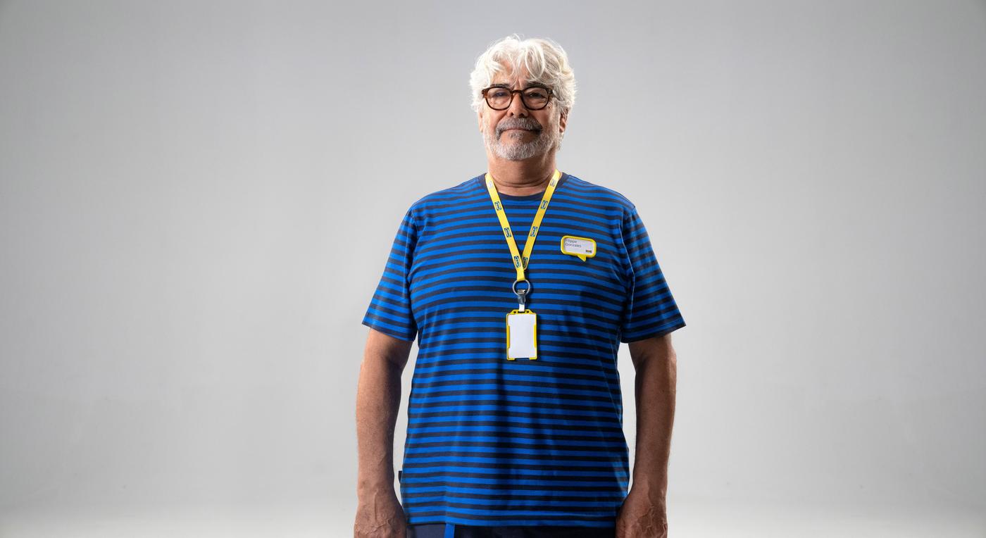 A man looks at the camera. He is wearing a striped t-shirt and a yellow lanyard.