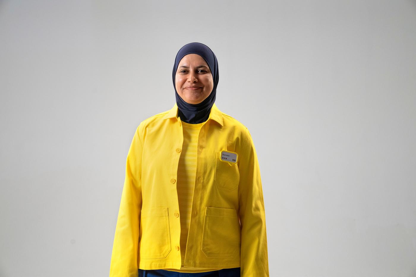 A woman smiles at the camera. She is wearing a yellow jacket, yellow top and black head covering.